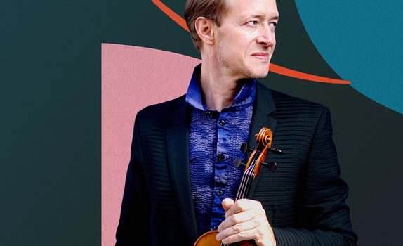 Anthony Marwood standing with his violin, in front of a dark background featuring blue and pink geometrical shapes.