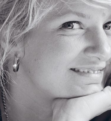Composer Andrea Tarrodi leaning forward with one arm resting on a surface and her face resting on the palm of her other hand.