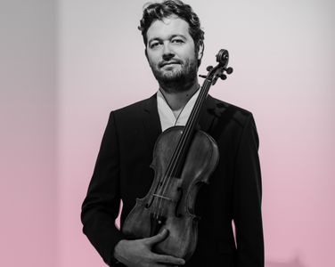 Lawrence Power holds his viola. He wears a black suit.