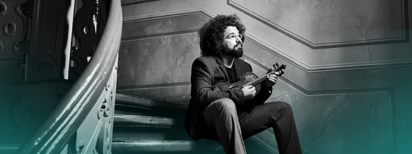 Jonian Ilias-Kadesha sits on some old stairs with a violin.