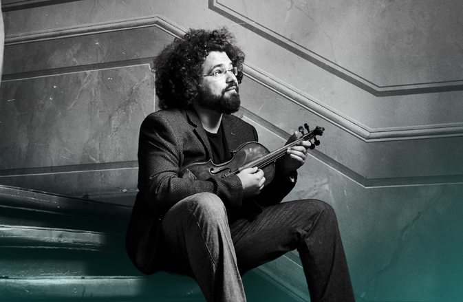 Jonian Ilias-Kadesha sits on some old stairs with a violin.