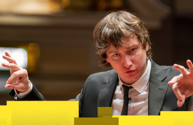 Maxim conducts in a black suit and white shirt.