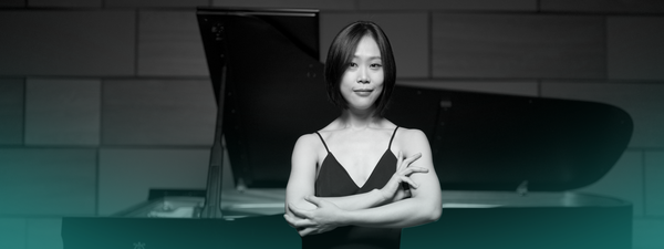 Yeol Eum Son stands in front of a piano with her arms crossed
