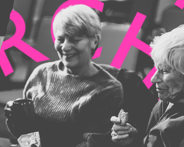 Two elderly people smile as they are served tea at the concert