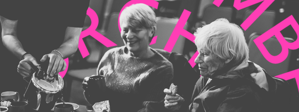 Two elderly people smile as they are served tea at the concert