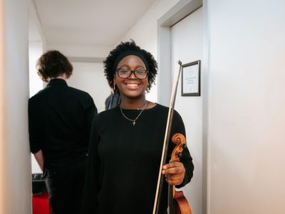 A young violinist smiles to the camera holding her instrument.