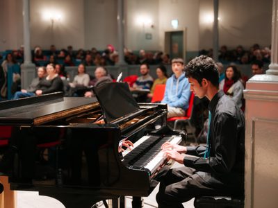 A boy plays the piano as the Queen's Hall audiences watches.