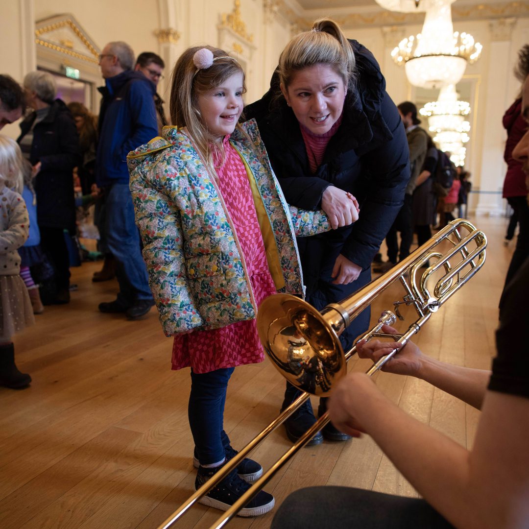 A child smiles at a trombone player with a parent