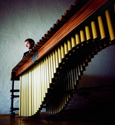 A marimba seen sideways on from a low angle, with Colin Currie just visible behind it