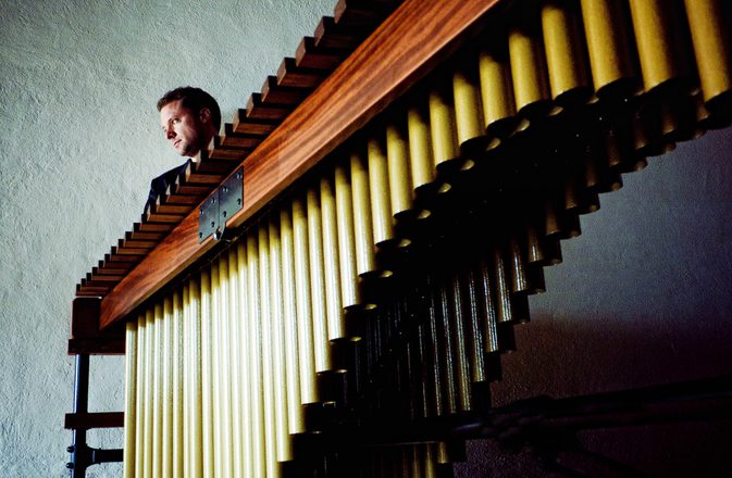 A marimba seen sideways on from a low angle, with Colin Currie just visible behind it