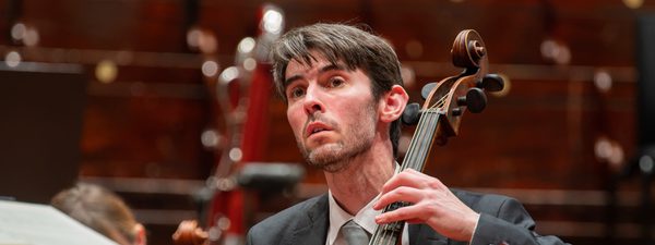 A man plays the cello, his bow on the string