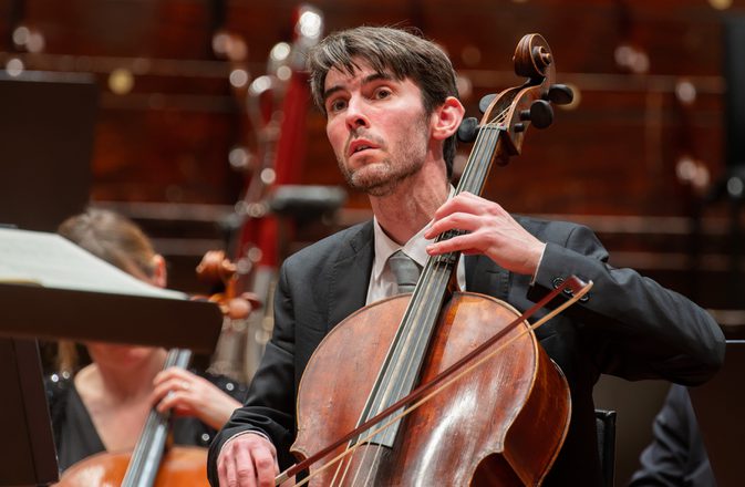 A man plays the cello, his bow on the string