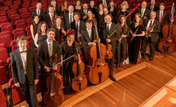 The Orchestra stand with Maxim with a concert hall backdrop