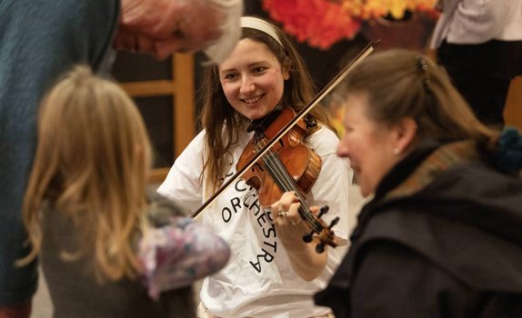 An SCO player with the Creative Learning team, demonstrates the violin to a child, as her grandparents watch.
