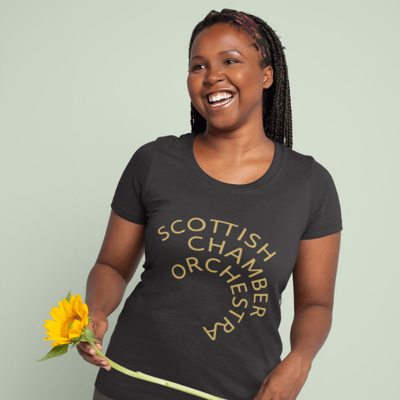 A black women wears a Black SCO tee and holds a flower smiling.