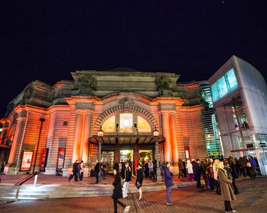 The main entrance of the Usher Hall in Edinburgh in the evening. The building is illuminated by light beams in the dark.