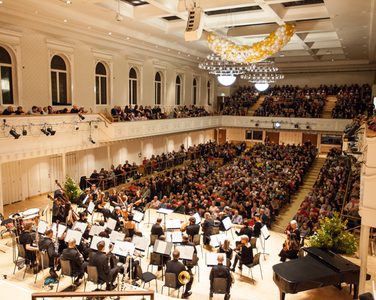 The orchestra take their seats on stage in front of the audience of a sold out concert.